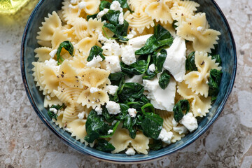 Farfalle pasta served with feta cheese and wilted spinach in a blue bowl, horizontal shot, middle...