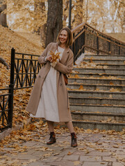 Beautiful blonde young woman in hat and coat walking on the stairs in the autumn park.