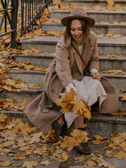 Beautiful blonde young woman in hat and coat sitting on the stairs in the autumn park.