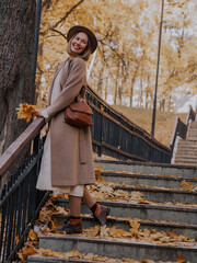 Beautiful blonde young woman in hat and coat walking on the stairs in the autumn park.