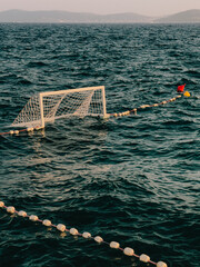 White water polo goal floating on calm sea during summer sunset, with lane ropes and colorful buoys...
