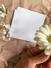 White paper in hand on beige backdrop with white flowers. white paper on the womans hand with copy space for your text. Dating notes, nice romantic backdrop. Vintage Saint Valentine background