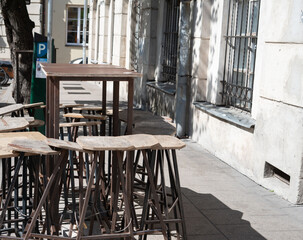 outdoor urban cafe setting with wooden stools and table amidst sunlit shadows and vintage architecture on a quiet city street, vibe, contrast, corner, arrangement, perspective, environment, serene