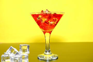 red cocktail glass with ice closeup shot on yellow background 