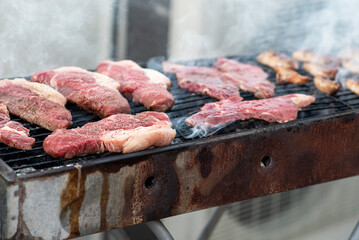 A barbecue grill filled with different cuts of meat, sizzling and smoking under the sun. Friends gather around, enjoying a summer cookout filled with delicious aromas.