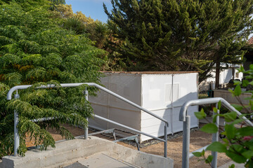 A traditional sukkah stands in a garden, surrounded by greenery, as people prepare for Sukkot festivities. The structure, simple yet inviting, adds to the seasonal atmosphere.