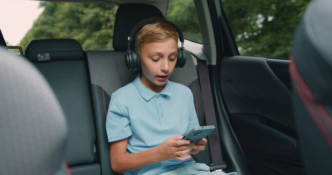 Teen boy singing songs to music from his phone playlist using earphones while driving in a car
