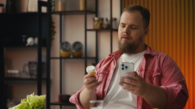 Large-bodied man holding weight loss pills, reading side effects on smartphone