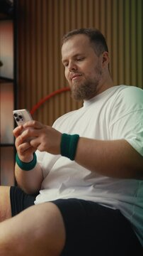 Large-bodied man using fitness app on phone during workout, tracking progress