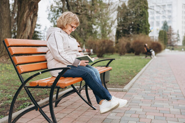Senior Woman Reading a Book on a Bench in a Park