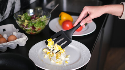 Beautiful young woman cooking vegetable scramble for breakfast in her kitchen early in the morning