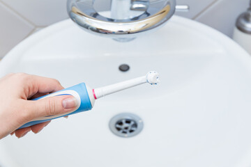 Hand holding electric toothbrush over clean bathroom sink