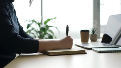 A woman writes in a notebook while seated at her office desk.