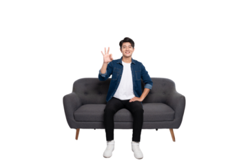 Full body image of young Asian man using phone sitting on sofa on PNG background	