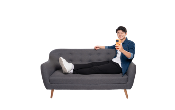 Full body image of young Asian man using phone sitting on sofa on PNG background	