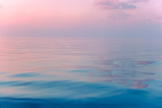Ocean waves horizon of Mirror surface in the evening, pastel color dusk. (Glass reflections ghosting included because the camera shot as lens penetrate the window)