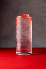 A beautifully crafted drink filled with ice and garnished with cherries sits elegantly on a vibrant red table, inviting guests to savor unique flavors in a gourmet restaurant
