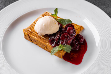 A luscious dessert featuring a slice of spiced cake topped with creamy ice cream, vibrant cherries, and a drizzle of cherry sauce, served elegantly on a fine dining plate
