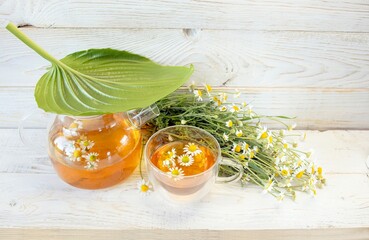 Herbal medicinal tea with chamomile flowers in a glass teapot, a bouquet of fresh flowers, on a...