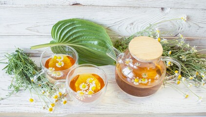 Herbal medicinal tea with chamomile flowers in a glass teapot, a bouquet of fresh flowers, on a...