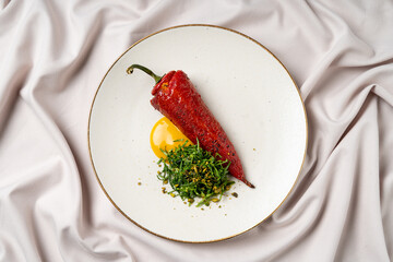 A beautifully plated dish features a stuffed red chili pepper resting on a pristine white plate