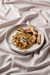 Savor the artistry of culinary creation featuring tender sautéed mushrooms topped with crispy bread. The presentation on luxurious fabric enhances the gourmet experience at a stylish dining setting