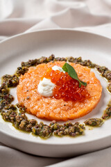 This exquisite dish features a perfect round of salmon tartare adorned with rich fish roe, creamy topping, and a distinctive herb sauce, elegantly styled on a fine plate