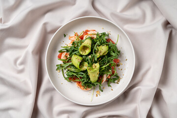 This culinary delight features a vibrant salad topped with juicy shrimp and arugula, garnished with green cucumbers. An artful presentation on a soft fabric backdrop captivates the senses