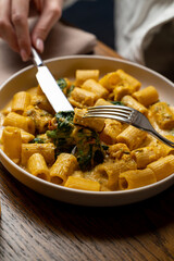 A hand skillfully cuts into a bowl of creamy pasta, adorned with fresh greens, showcasing a fusion of texture and flavor perfect for savoring gourmet cuisine moments