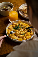 A person savoring a plate of creamy pasta with spinach, accompanied by a refreshing orange drink. The inviting ambiance enhances their dining experience