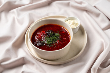 A rich bowl of borscht displays vivid red hues, garnished with leafy herbs and served alongside a small dish of creamy goodness. This culinary delight invites a feast for the senses