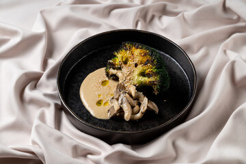 Roasted broccoli with savory sauce and delicate mushrooms elegantly arranged on a dark plate, showcasing exquisite culinary artistry