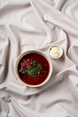 A bowl of rich borscht, deep red and garnished with fresh herbs, sits elegantly on a soft, textured fabric