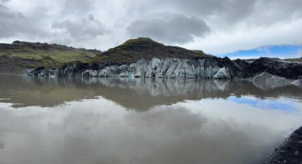 Panoramic view of the retracting Solheimajokull glacier and its reflection in the water of the glacial lagoon