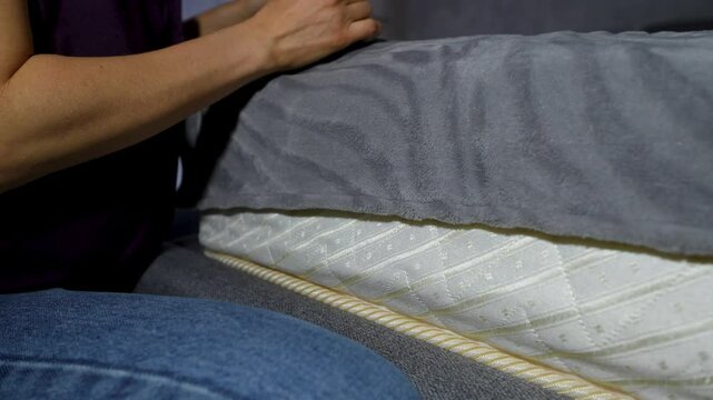 Close-up of a person taking a stack of US hundred-dollar bills under a mattress