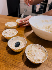 Muffin mixture scooped by hand into liners, muffin texture filled with oats and blueberries, muffin prep at home highlights healthy and cozy recipe, easy breakfast. Cupcake made of oats and fruits