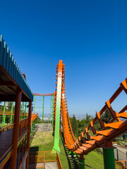 Fototapeta premium Orange roller coaster at an amusement park with cloudy blue sky, vertical photo for social media, copy space. High quality photo