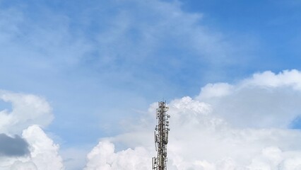 Obraz premium Telecommunication Tower Against a Blue Sky with Puffy Clouds