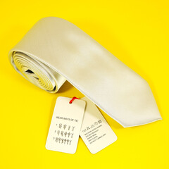 plain fabric necktie rolled on yellow background closeup view with tags 