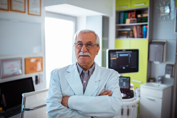 Confident senior doctor standing in modern medical office with arms crossed