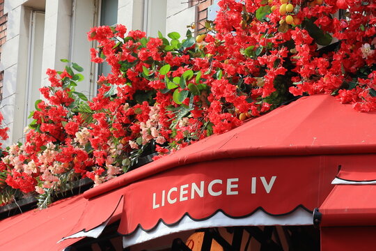 "Licence IV" inscrit en fran&ccedil;ais sur le store banne rouge d&rsquo;un caf&eacute; / bar / bistrot / restaurant / brasserie &agrave; Paris, avec des fleurs artificielles rouges (France)