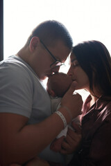 mom dad newborn baby at bright window together