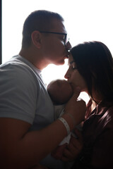 mom dad newborn baby at bright window together