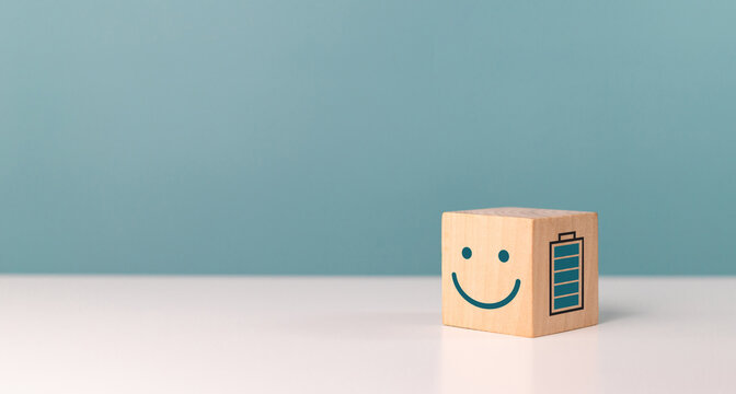 Work motivation, mental health assessment, battery, energy, employee happiness and positive attitude. Wooden block with smile face emoticon with full level energy battery in the office