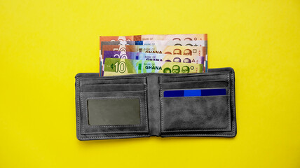 Mens wallet with Ghanaian Cedis money currency notes inside lying isolated on yellow background
