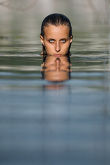 Fototapeta premium Woman Submerged in Calm Water with Intense Reflection and Focused Gaze..