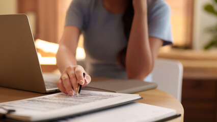 Asian woman hands are signing papers on desk with laptop. Adult female reviews business contract...