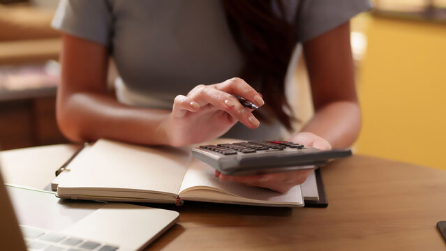 Asian woman's hands using calculator with notebook for finance management Calculating budget expenses with pen sitting on desk.