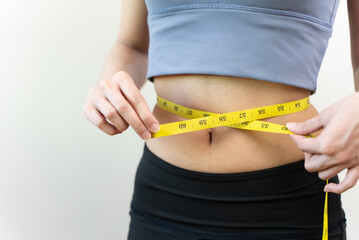 Young slim woman measuring her waist by measure tape after a diet