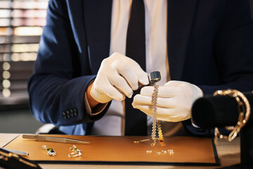 Appraiser with loupe evaluating luxury jewelry at table, closeup